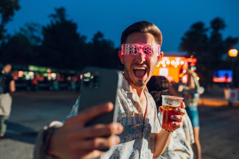 Young man taking a selfie at a music festival while holding a beer